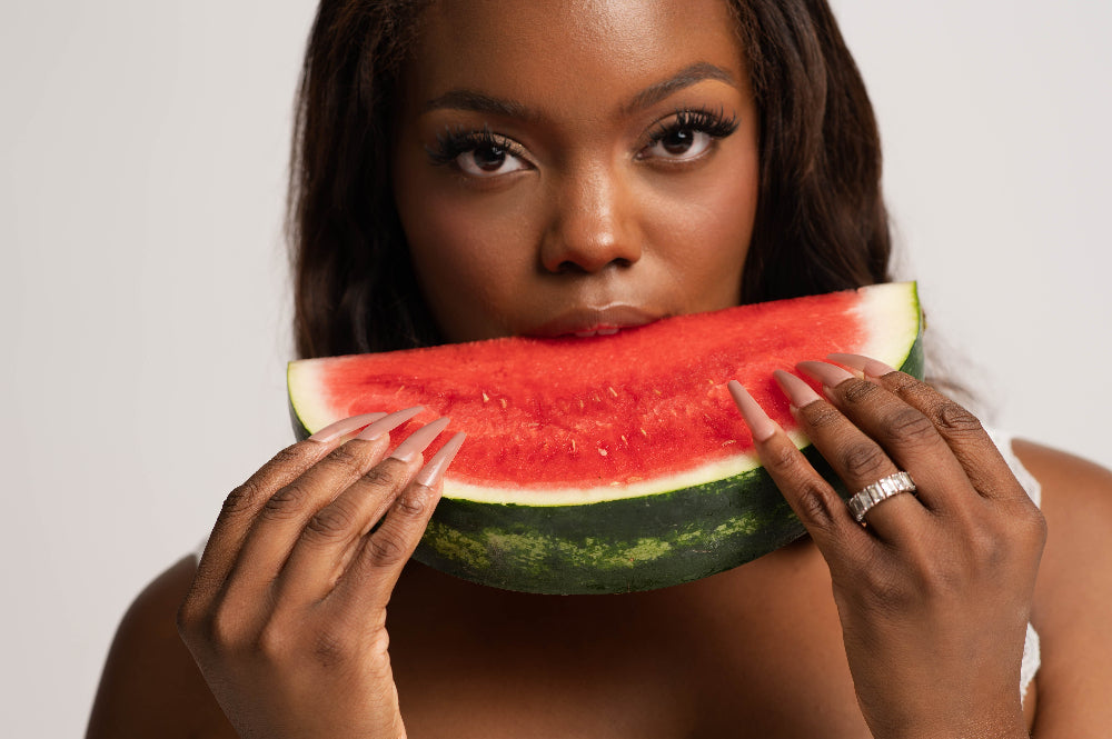 Woman holding a watermelon slice in front of her face against a plain background