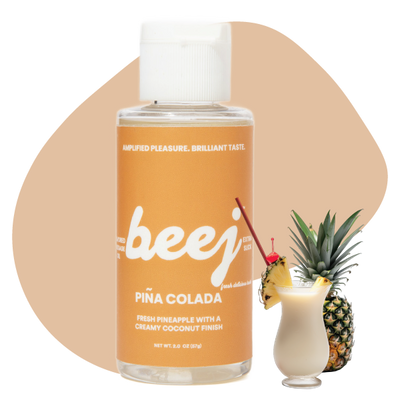 Beej Pina Colada edible massage oil with a cocktail and pineapple on a beige background